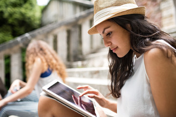 Teenage student with tablet sitting on stone steps.