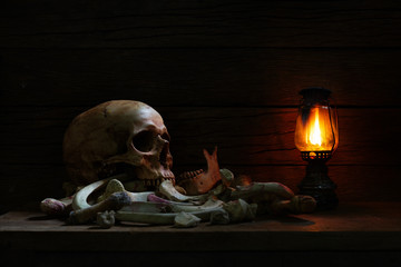 Pile of bone and skull on dark background with lantern on plank / Still life style and dim light