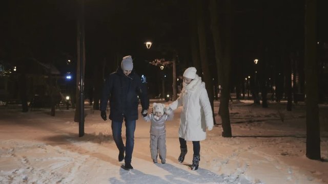 Cute young family is walking in a winter evening park