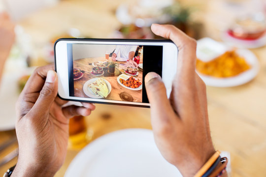 hands with smartphone picturing food at restaurant