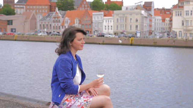 Pretty young woman spending time outdoors, drinking wine and enjoying city river