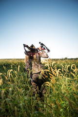 Hunter with bow walking through tall grass