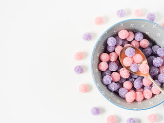 Round purple and pink bonbon candies sweets in gray bowl on white canvas background. Minimal still life