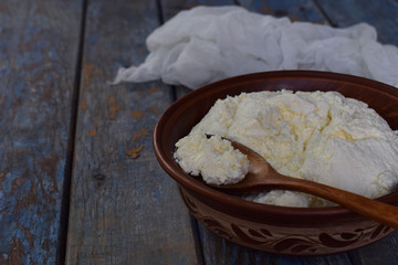Cottage cheese from curdled milk or yoghurt in a clay bowl on a wooden background