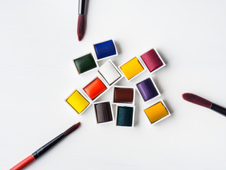 Naklejka premium Watercolor godets and brushes on white background. Flat lay. Copy space