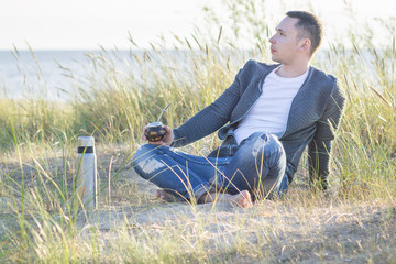 Naklejka na ściany i meble Young man drinking yerba mate on the Baltic sea coast