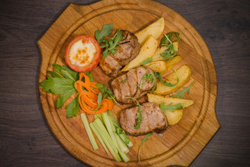 Three pork steaks with fried potatoes and vegetables on a wooden background