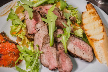 Roasted meat with blood in a cut with vegetables on a wooden background