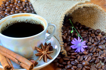 A cup of black coffee with cinnamon bark and anise star among the sackcloth, whole grains of coffee...