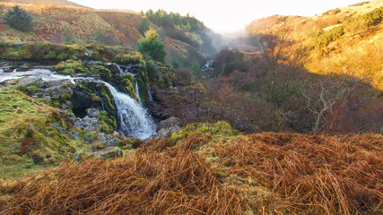 Waterfall flowing into a misty Scottish glen