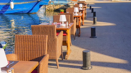 Row of tables and wicker chairs with lamps beside the water in a marina