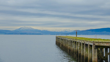 Fototapeta premium Derelict pier on the Firth of Clyde with snow covered mountains in distance
