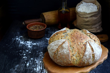 A loaf of homemade bread from whole grain flour and flax seeds on a dark wooden background. Copy space. Photographing with natural light