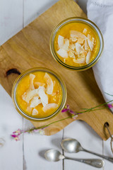 Black rice pudding with mango and coconut flakes in the glass jar.  White background, wooden table.