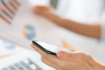 Business woman hand with Financial charts and mobile phone over laptop on the table .