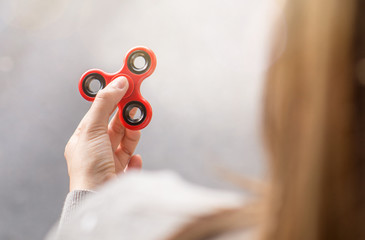 Woman or girl holding red fidget spinner in hand on a sunny summer day in city.