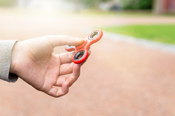 Woman or girl holding red fidget spinner in hand on a sunny summer day in a park outside.