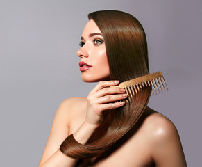 A beautiful young girl with long shiny silky hair sits and combs her hair with a golden comb. Cosmetics for hair, care, spa, beauty, fashion. Beauty saloon. Smooth skin. Advertising. Radiance, shine.