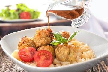 Pouring tasty sauce into bowl with turkey meatballs and pasta, closeup