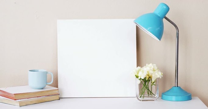 Stack of books, blank board, flower vase, cup of tea and table lamp