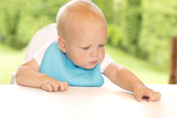 Serious blonde toddler in a blue bip sitting at the table. Outdoor shot