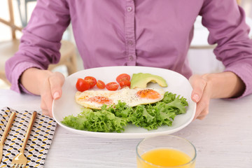 Woman holding plate of fried eggs and vegetables on table