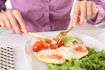 Woman eating tasty breakfast with fried eggs on white table