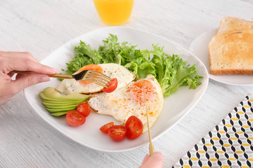 Woman eating tasty breakfast with fried eggs on white table