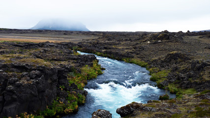 reißender Fluss in karger Lavalandschaft mit Blick auf Vulkan Hekla in Island