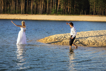 Młodzi ludzie chlapią się wodą na brzegu jeziora, ślub, wesele. - obrazy, fototapety, plakaty