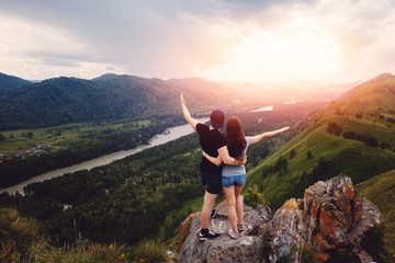 team of friends: A guy and a girl in love with tourists stand and hug at the edge of the cliff, raise their hands up - rejoice. Concept travelers.