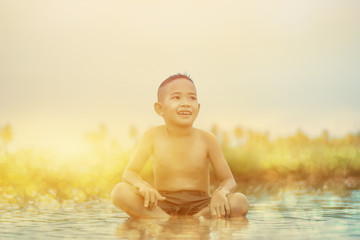 Asian Boy playing in water loosen hot looks happy, Before sunset background ,Thailand.