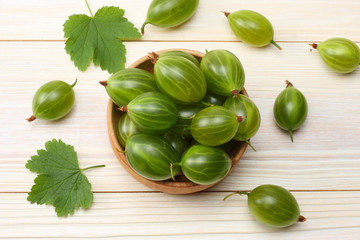 Gooseberry in wooden bowl on white wooden background.