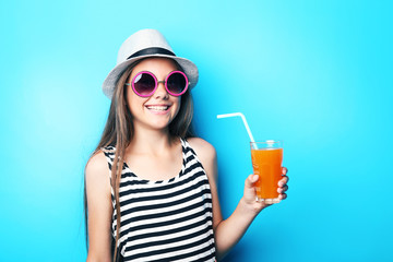 Portrait of beautiful girl with sunglasses and glass of juice on blue background