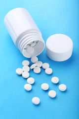White pills in plastic bottle on blue background