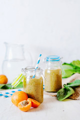 Healthy food, summer drinks, fruit and vegetable smoothie with banana, apricot and spinach in glass bottles on a light background, detox