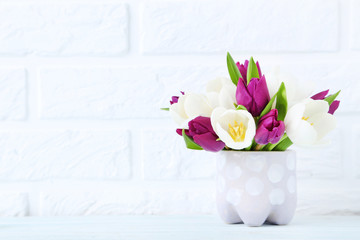 Bouquet of tulips in cup on brick wall background