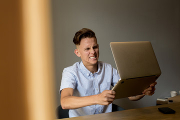 Very angry and annoyed young man slams expensive technology laptop on table, because does not understand information on screen, typical internet meme