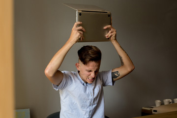 Very angry and annoyed young man slams expensive technology laptop on table, because does not understand information on screen, typical internet meme