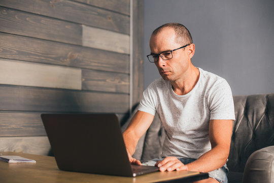 Concentrated and serious businessman in casual outfit leads important negotiations from home office, wearing computer glasses to work on laptop