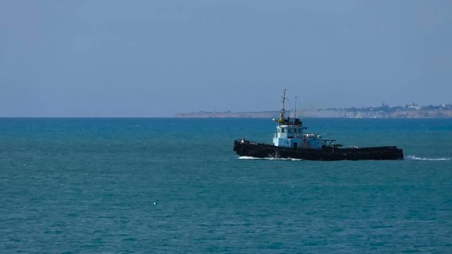 The motor boat is moving along the shore. Tugboat sails on the black sea.