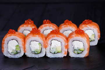 Sushi rolls with salmon, avocado and cream cheese, decorated with red caviar, served on black slate. Japanese food, restaurant menu
