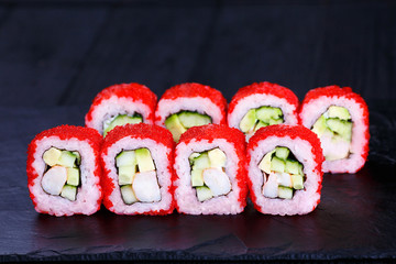 Delicious sushi roll with avocado, cucumber and cream cheese, covered with red caviar, served on black slate. Tasty japanese cuisine