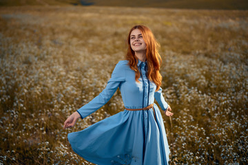 Beautiful young woman in a blue dress in a field of flowers in the mountains