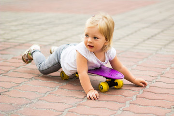 A little girl is lying on a skateboard. He studies riding on the street.