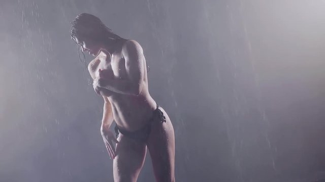 girl fitness model stands at night in the fog and in the rain. she's in shorts covers a large silicone breast hand
