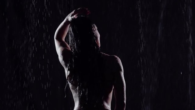 sexy middle-aged woman standing in the bathroom with his back to the camera. she enjoys the water jets depending on layer thickness on the soft skin. corrects long black hair