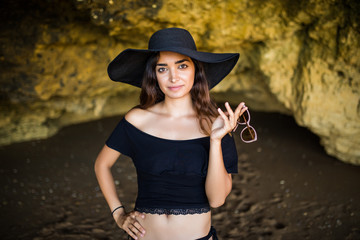 Happy Beautiful mexican woman with hat and sunglasses sunbathing on rocks beach on summer vocation time