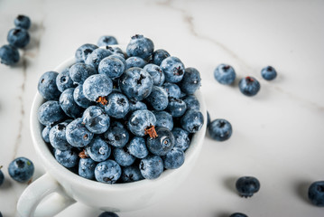 Fresh raw organic farm blueberry in white cup on white marble kitchen background, copy space