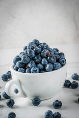 Fresh raw organic farm blueberry in white cup on white marble kitchen background, copy space
